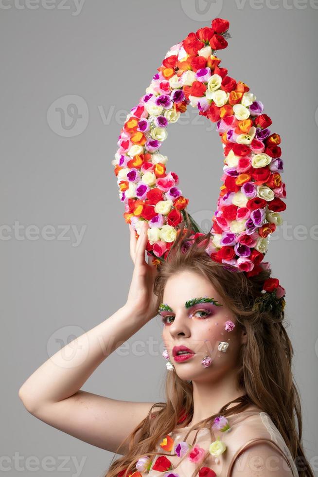 Beautiful girl with flower horns. Spring model. Beautiful girl with an unusual make-up. Hairstyle with flowers. Fantastic portrait of a beautiful woman. Summer fairytale woman. Malificent style. photo