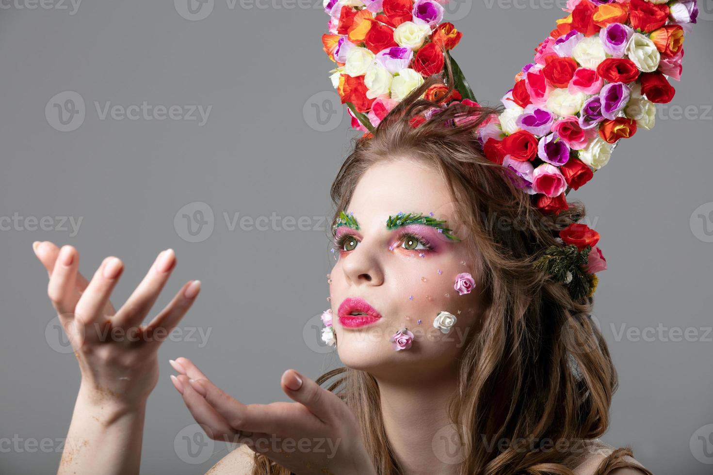 Beautiful flower girl with horns. Goddess Flora. Beautiful woman with fantastic makeup is blowing. Spring girl model. photo