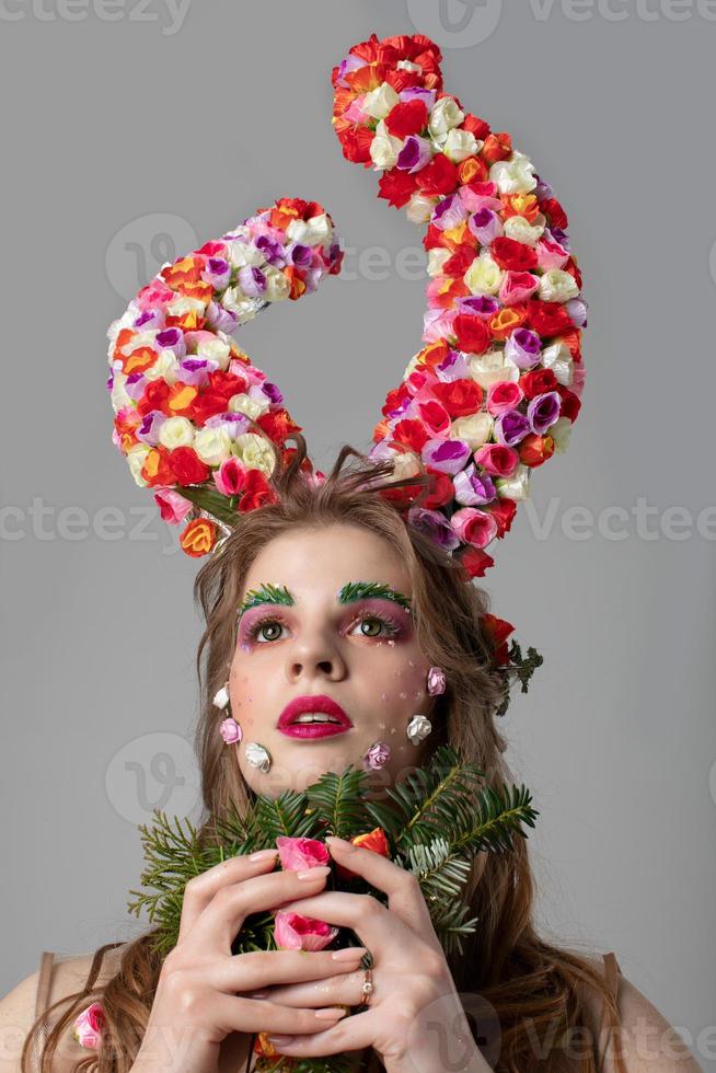 Portrait of a beautiful girl with flower horns. Goddess Flora. Beautiful woman with fantastic makeup and a forest bouquet. Spring girl model. photo