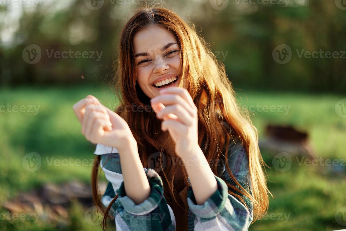 A beautiful woman outdoors in a green park laughs and smiles as she looks into the camera at sunset in the sun. Close-up portrait photo