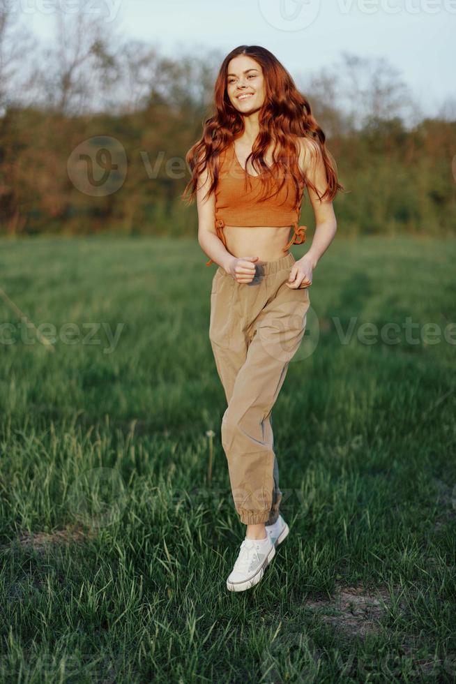 A woman works out and runs through the field in the park with a smile in a good mood looking at the beautiful summer nature around her photo