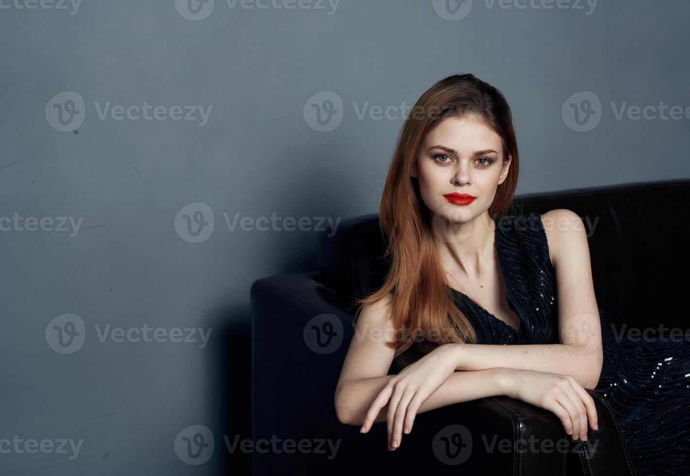 Elegant woman in a dark dress on a leather sofa and evening makeup photo