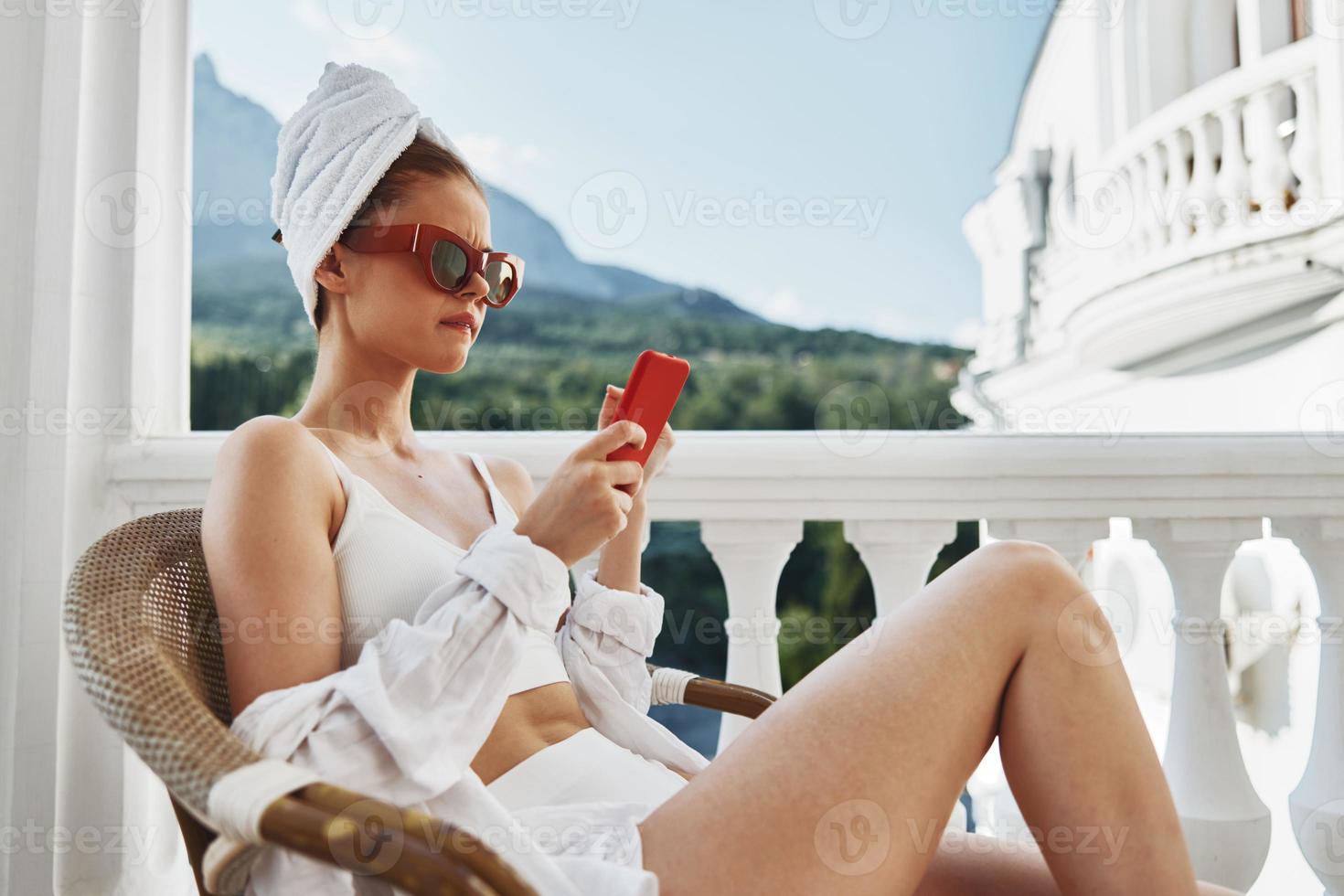 retrato de joven mujer con un rojo móvil teléfono sentado en el balcón perezoso Mañana foto