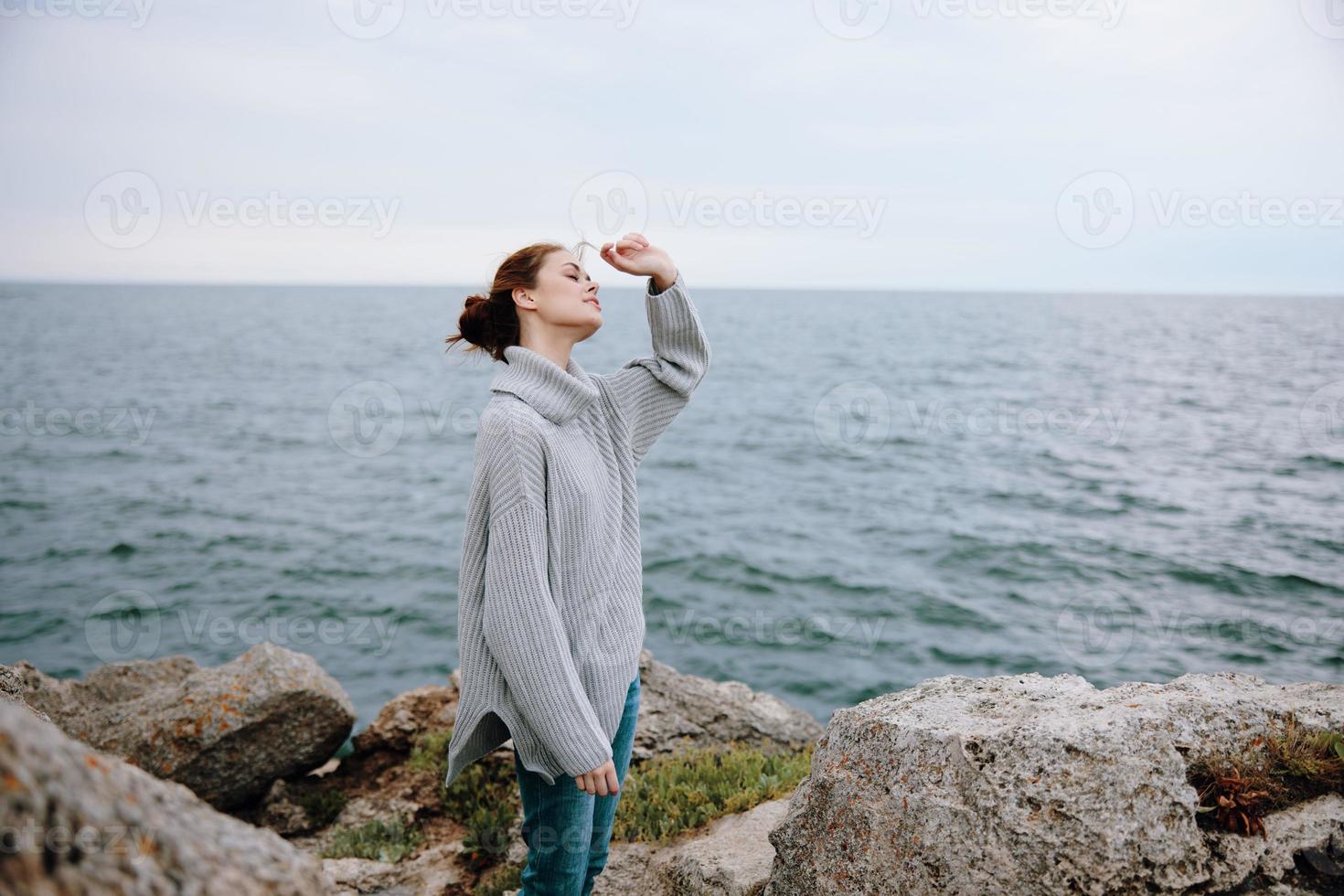 portrait of a woman in a gray sweater stands on a rocky shore nature Lifestyle photo