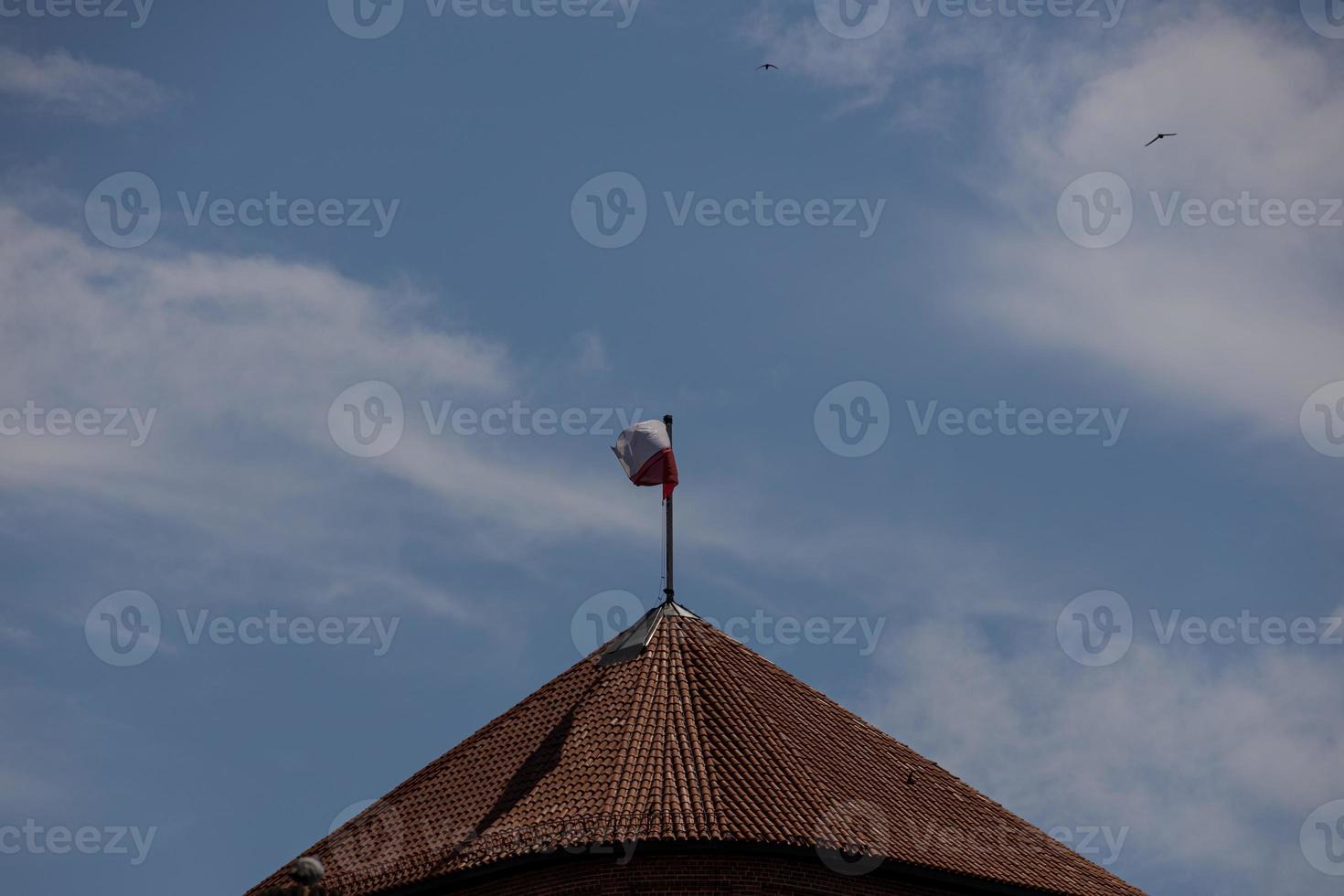 poland red and white flag on roof of tiled building in blue sky background photo
