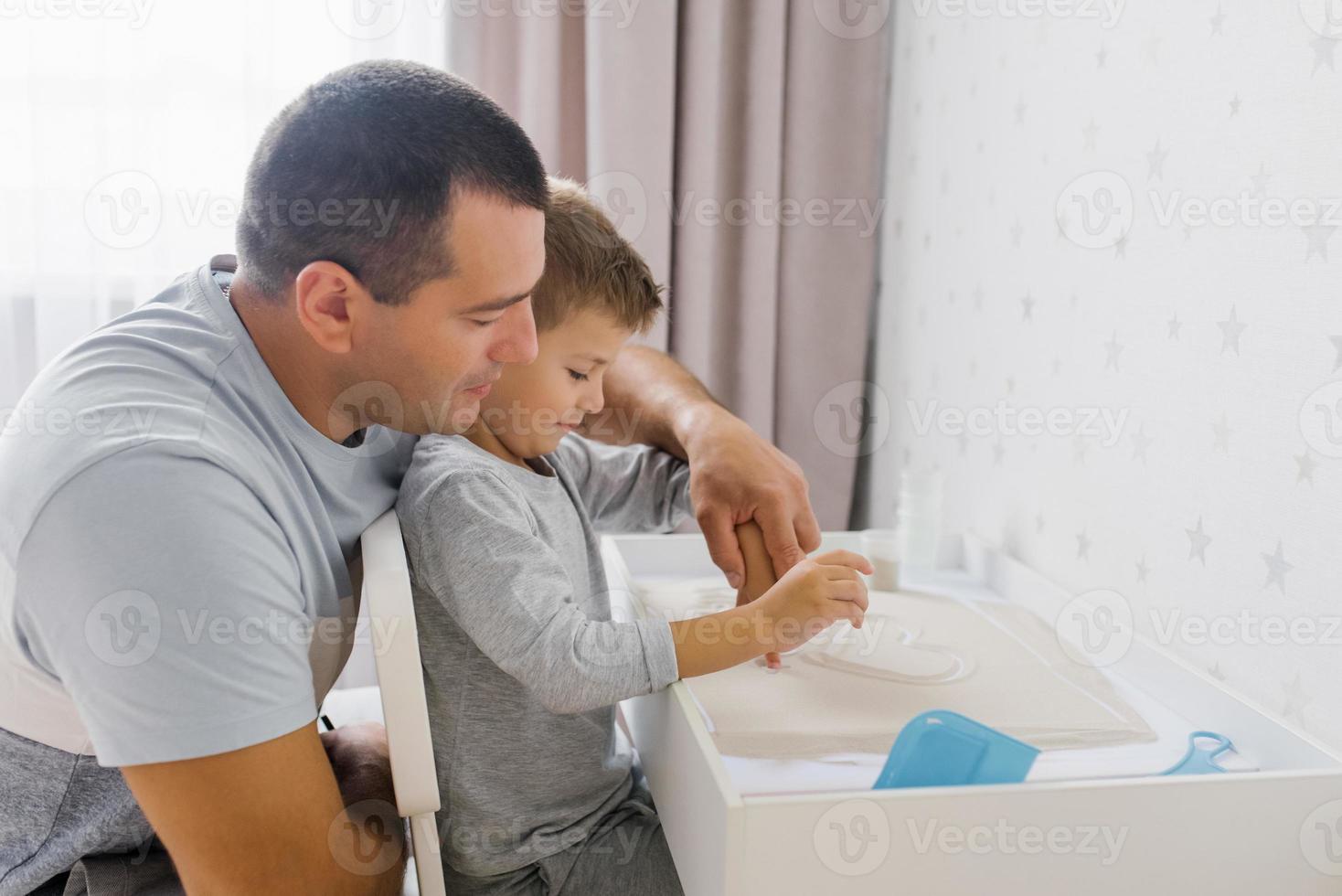 Dad and his baby son play at home with quartz sand photo