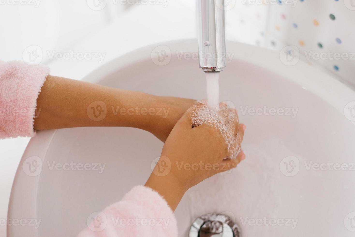 Close up view of young child washing hands with soap in sink photo