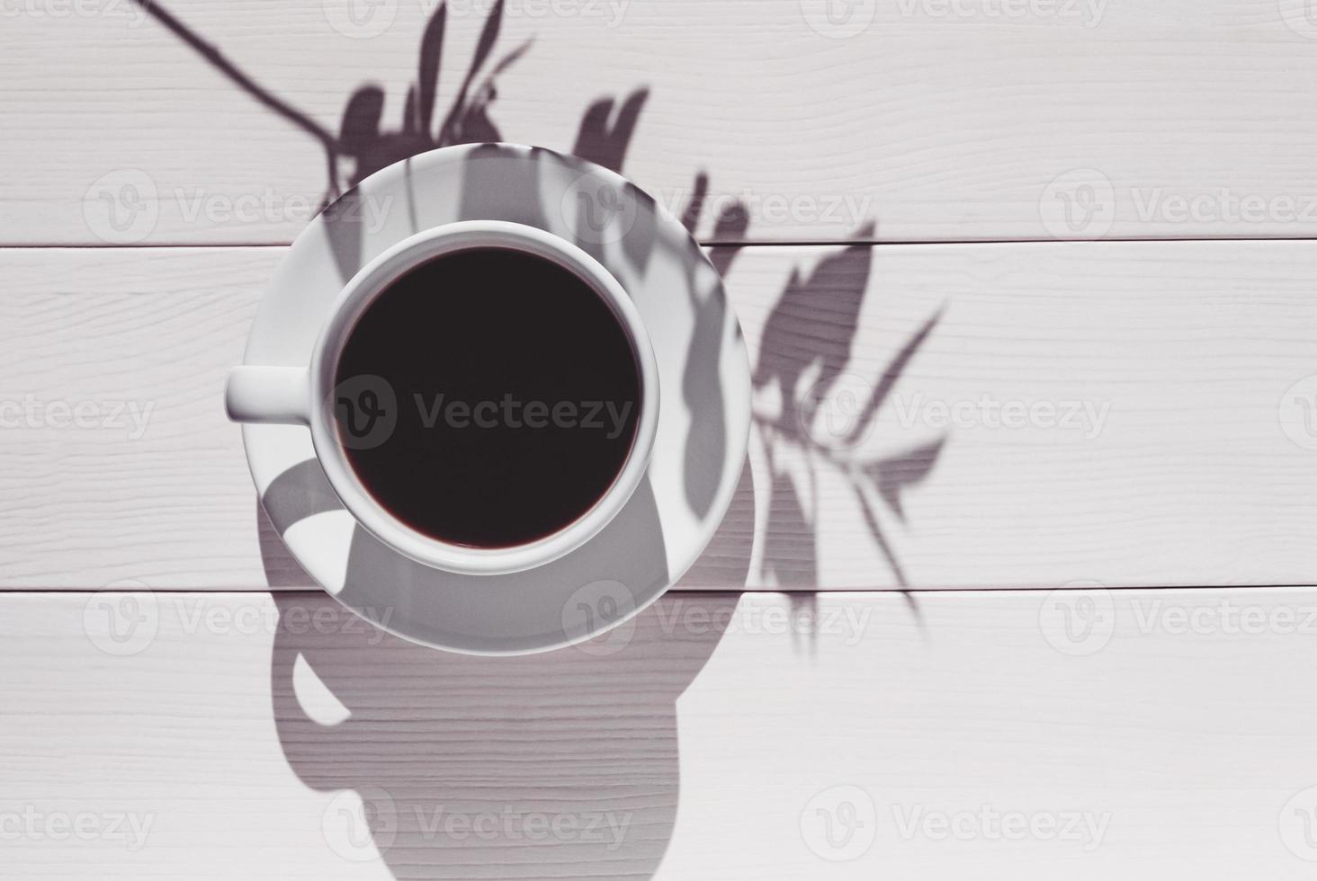 Coffee cup on wooden table with a shadow of plant branch, high angle view photo