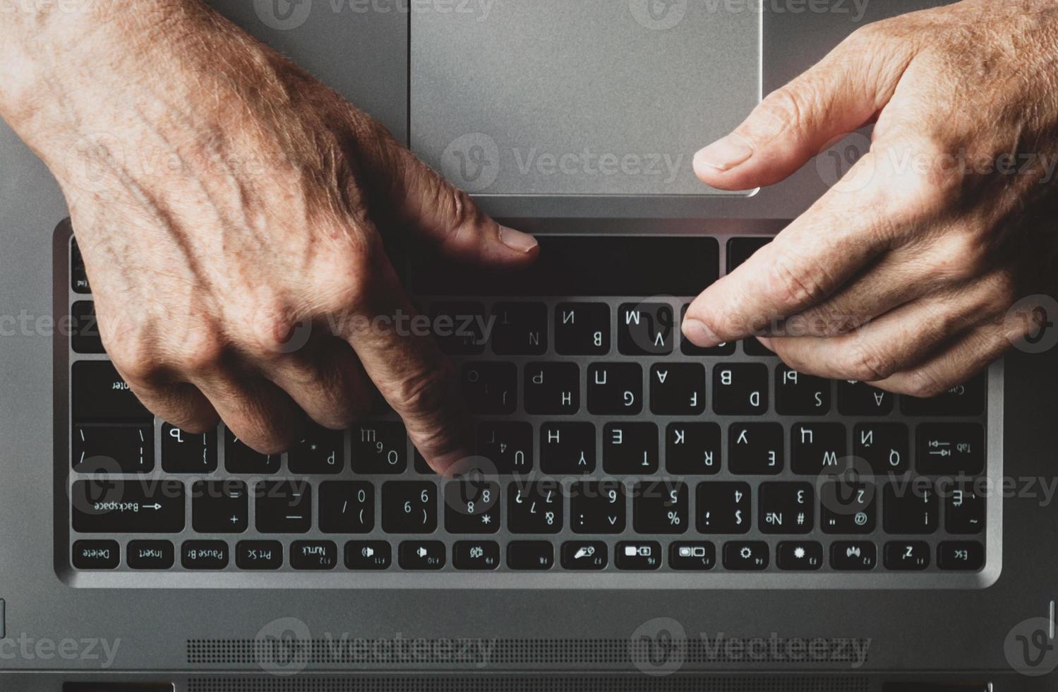 Hands of an elderly man learning to use computer, typing on a laptop, view from above photo
