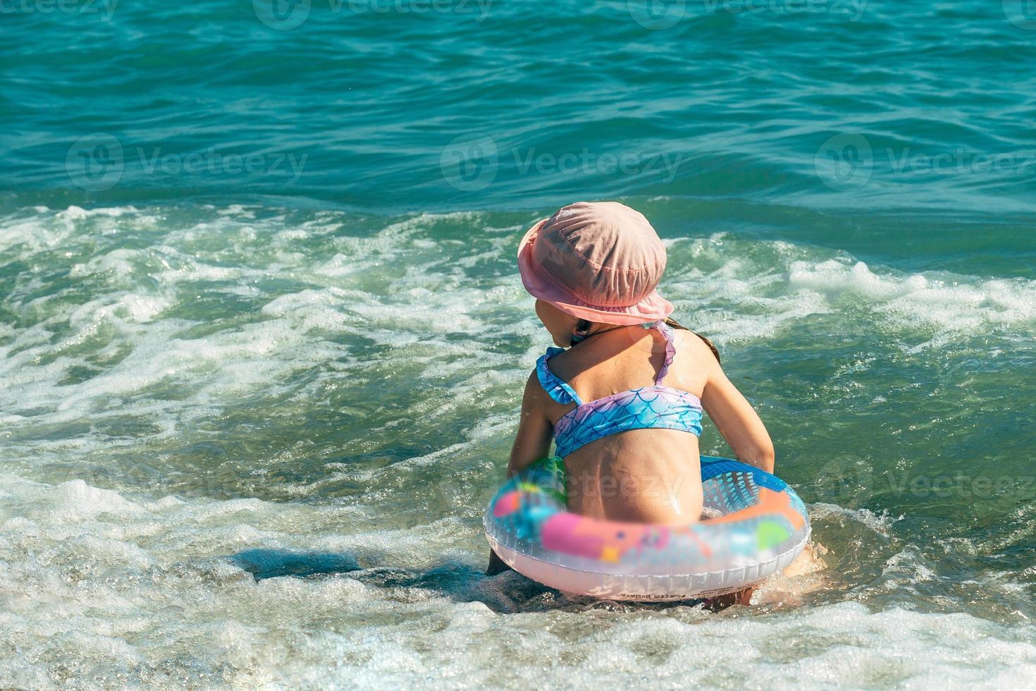 a cheerful preschooler girl in a swimsuit and a sun hat with an inflatable ring has fun swimming on a sunny day in the sea photo