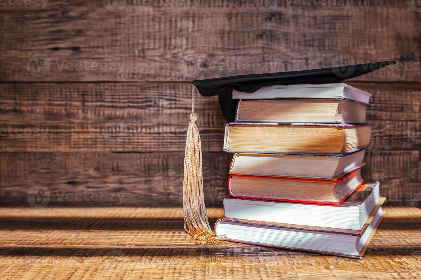 un académico gorra mentiras en parte superior de un apilar de libros en un de madera antecedentes. graduación y graduación concepto foto