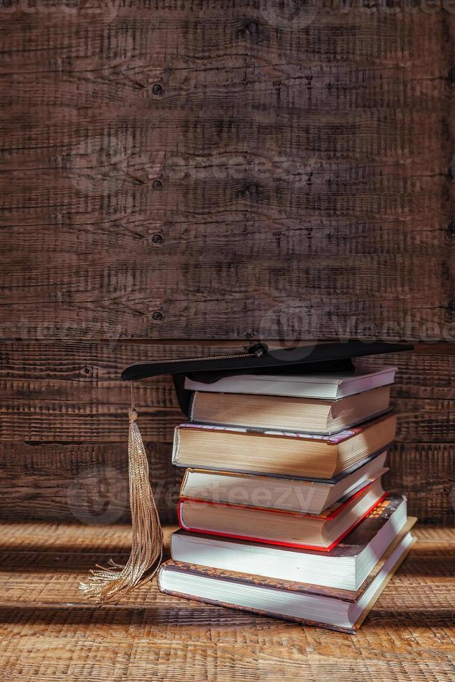 an academic cap lies on top of a stack of books on a wooden background. Graduation and graduation concept photo