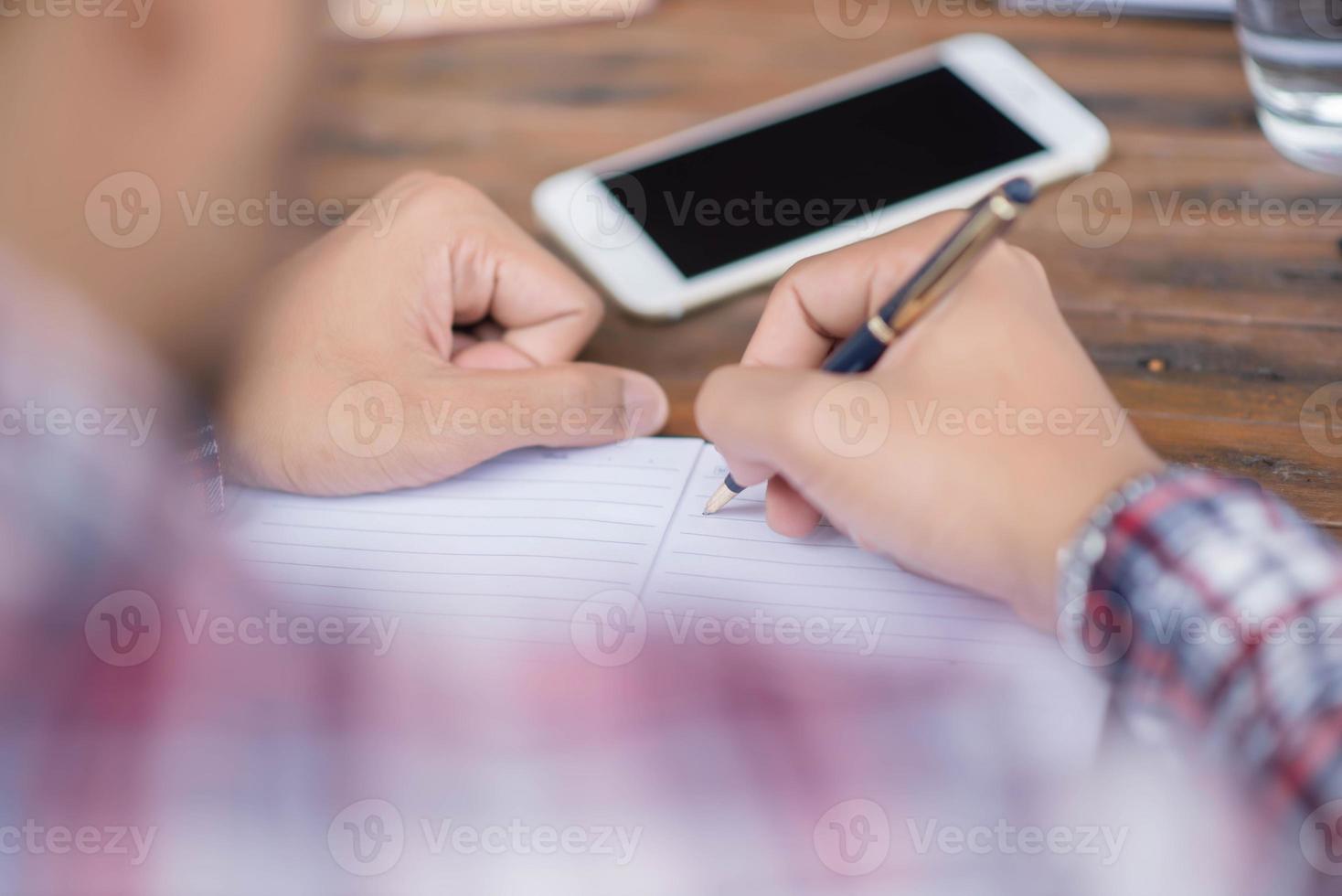 A business man is taking notes into a notebook with a telephone and an alarm clock on the table when the morning light. photo