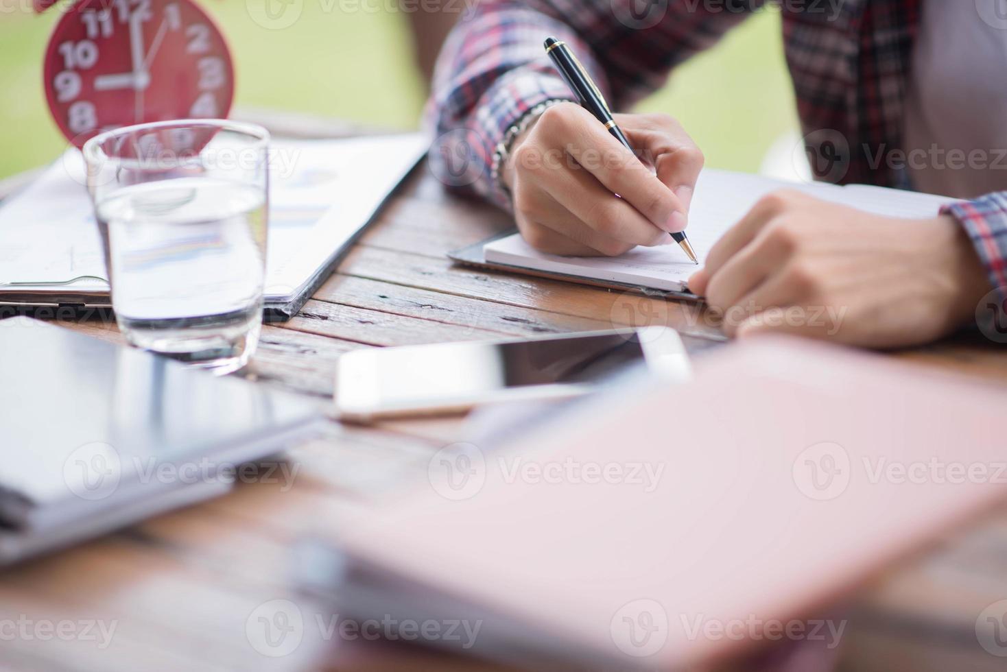 A business man is taking notes into a notebook with a telephone and an alarm clock on the table when the morning light. photo