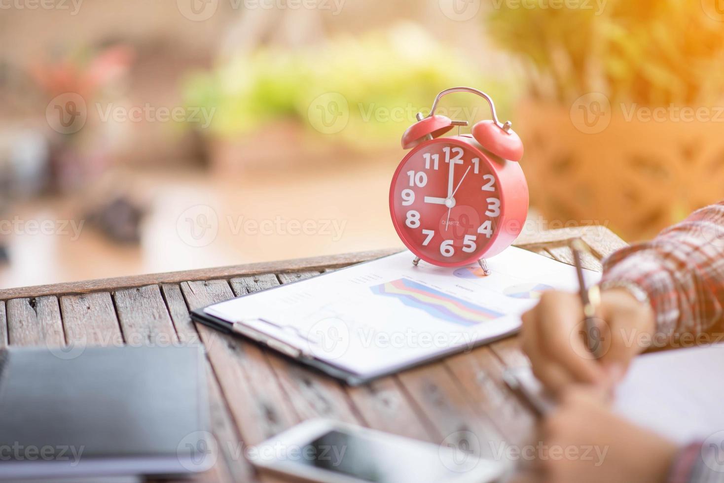 A business man is taking notes into a notebook with a telephone and an alarm clock on the table when the morning light. photo