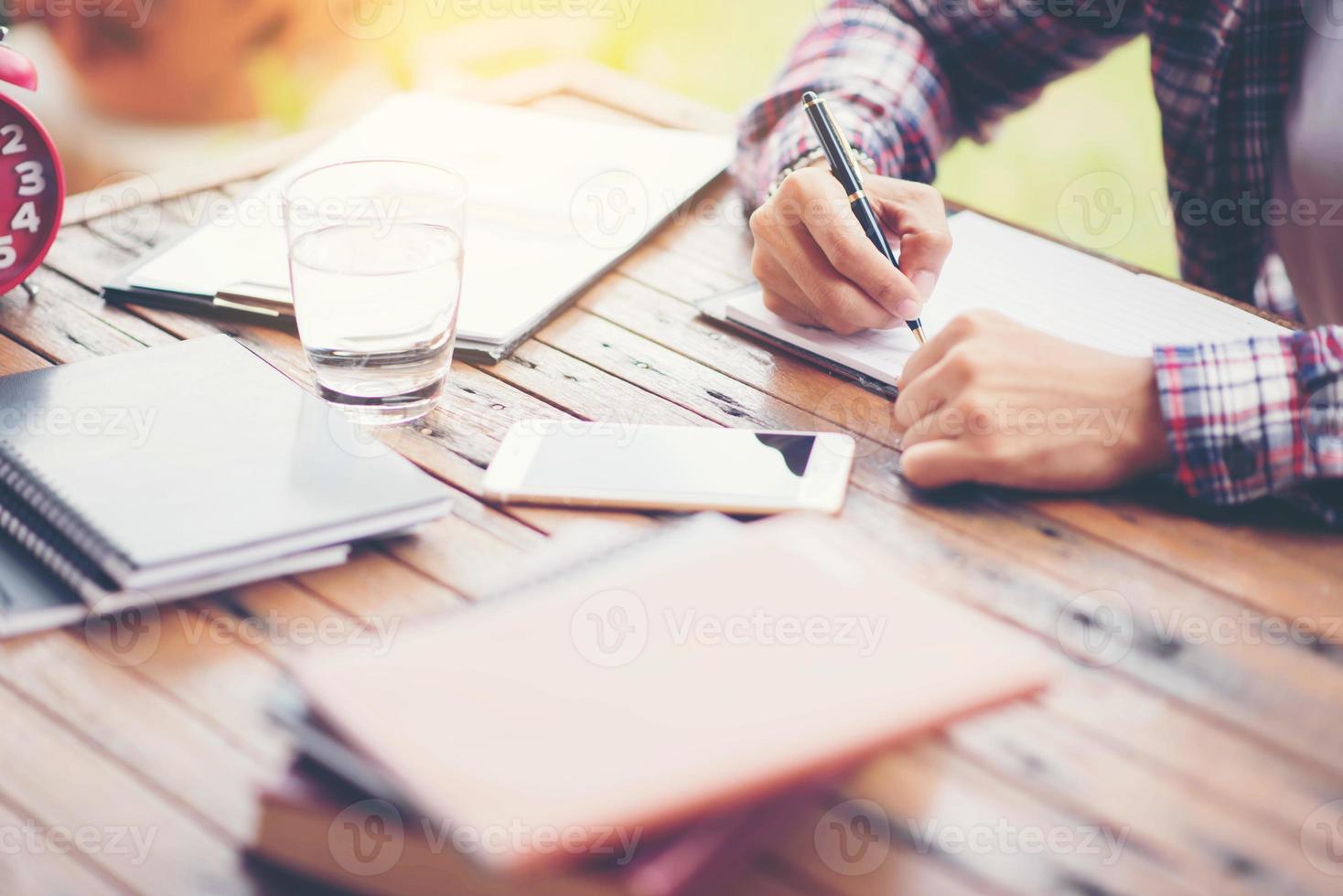 A business man is taking notes into a notebook with a telephone and an alarm clock on the table when the morning light. photo