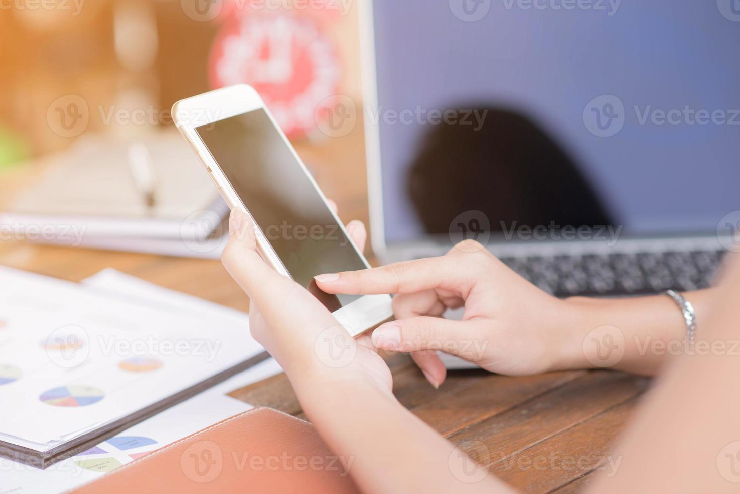 Young businesswoman hard at work at her desk writing notes on a pad from her laptop computer with analytical charts and graphs in front of her, high angle view photo