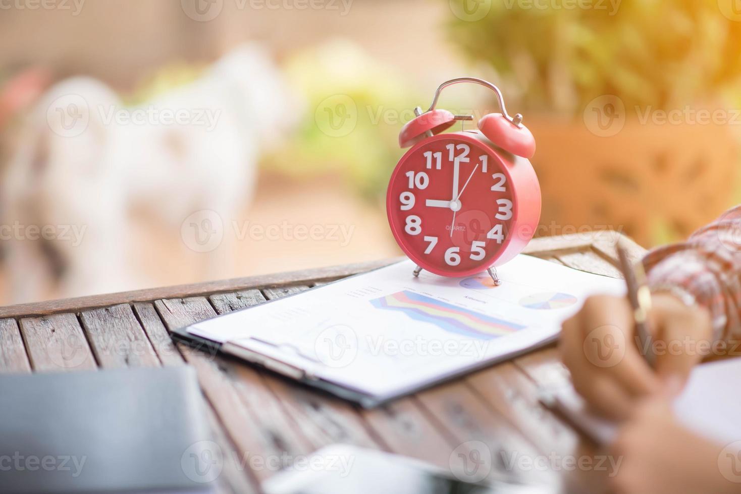 A business man is taking notes into a notebook with a telephone and an alarm clock on the table when the morning light. photo