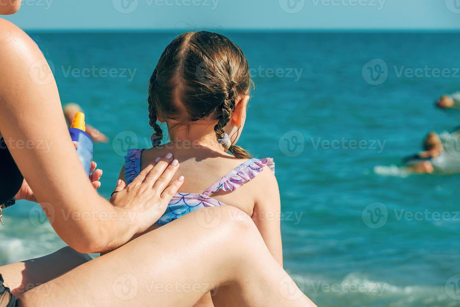 Mom carefully smears her child's skin with a protective cream on the beach. Skin care and sun protection. Sunscreen spray for children. photo