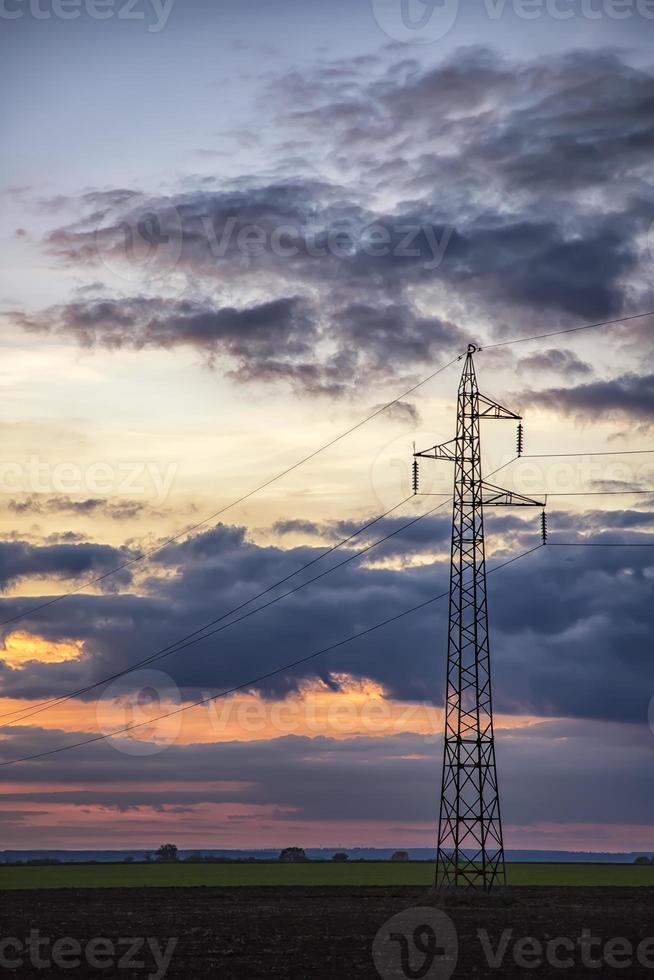 Poles and overhead power lines silhouettes in the dusk. Electricity generation and distribution. Electric power industry and nature concept photo