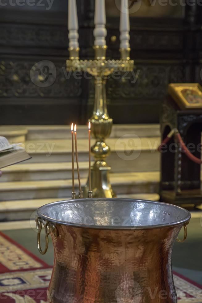 bautizo en el iglesia. Iglesia utensilios en el ortodoxo iglesia. un grande cuenco de agua para el bautismo de un bebé con cera velas foto
