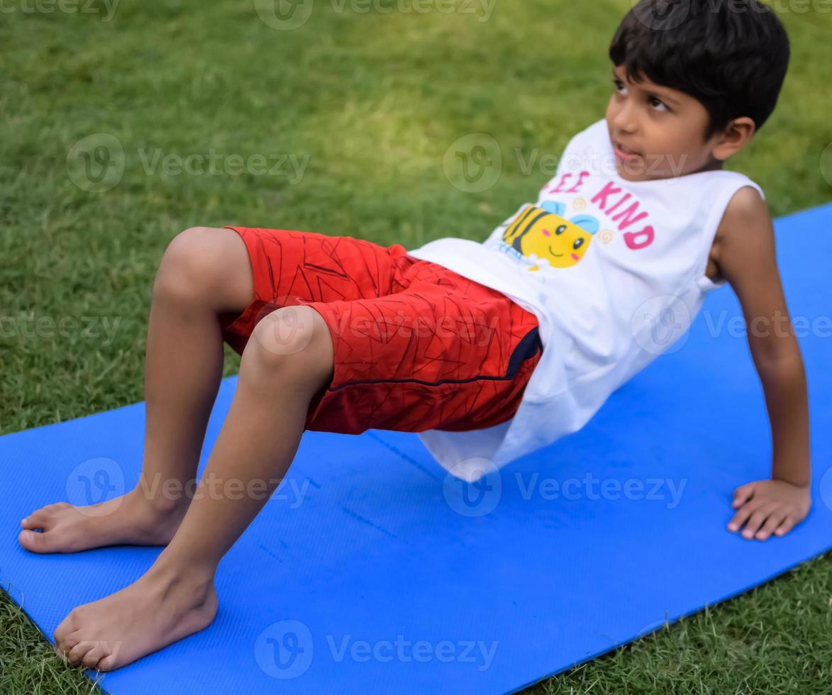 asiático inteligente niño haciendo yoga actitud en el sociedad parque exterior, para niños yoga pose. el pequeño chico haciendo yoga ejercicio. foto