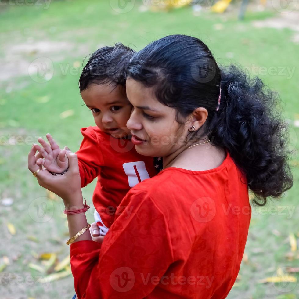 Loving mom carrying of her baby at society park. Bright portrait of happy mum holding child in her hands. Mother hugging her little 9 months old son. photo