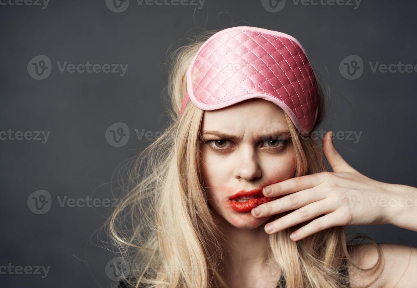 A blonde with bright makeup on her face and a pink sleep mask on her head photo