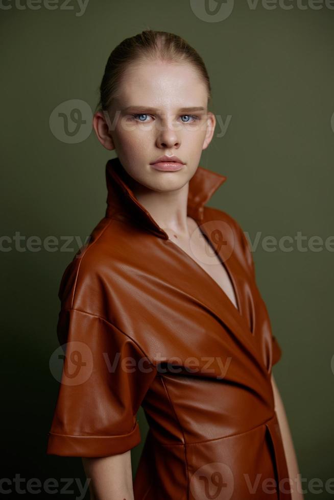 Elegant fashionable young blonde girl with blue eyes with evening makeup in a leather dress looks at the camera posing isolated for banner design. Studio portrait on a green background. Makeup concept photo