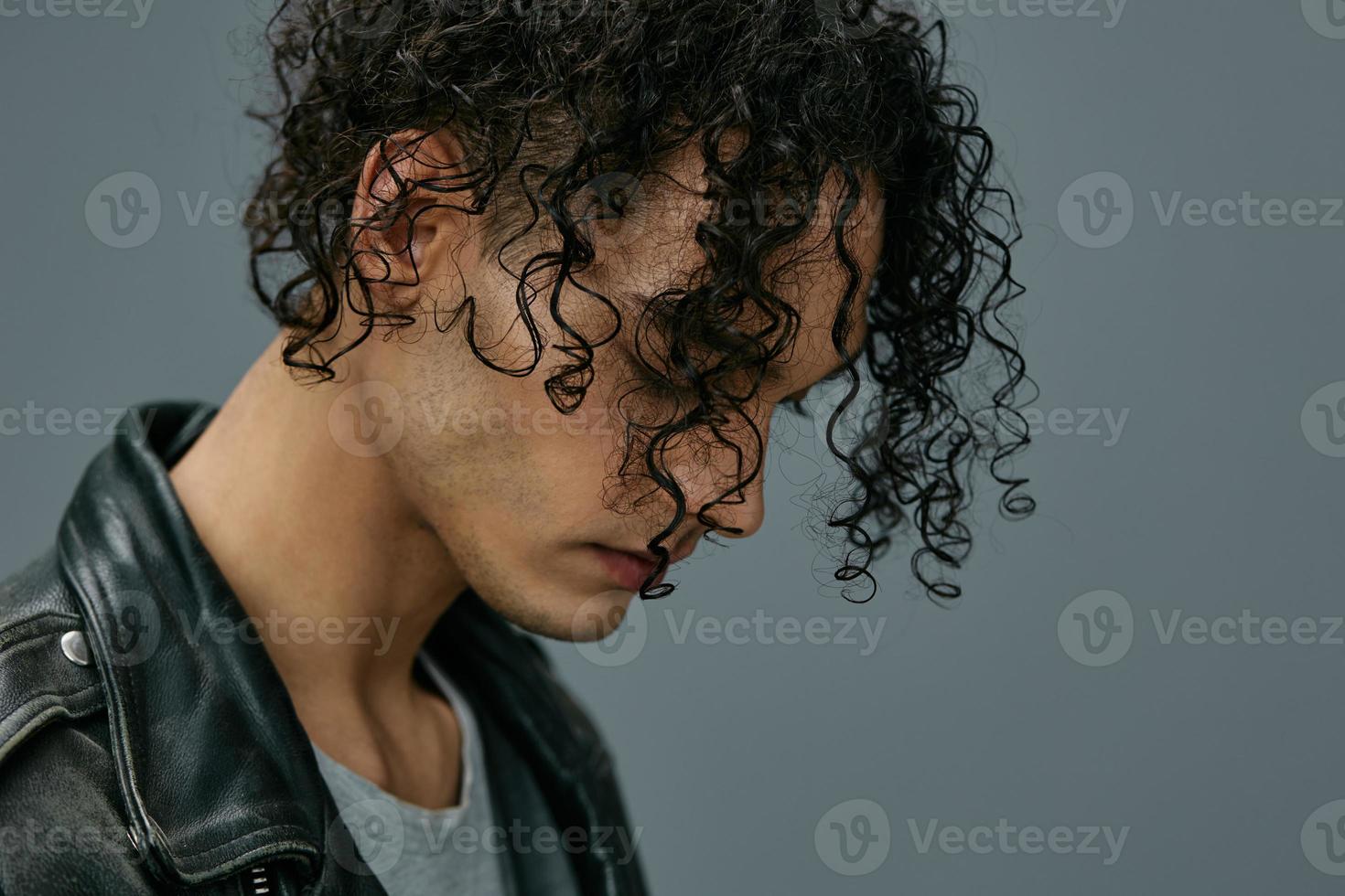 Headshot portrait of handsome stylish tanned curly man leather jacket posing isolated on over gray studio background. Cool fashion offer. Huge Seasonal Sale New Collection concept. Copy space for ad photo