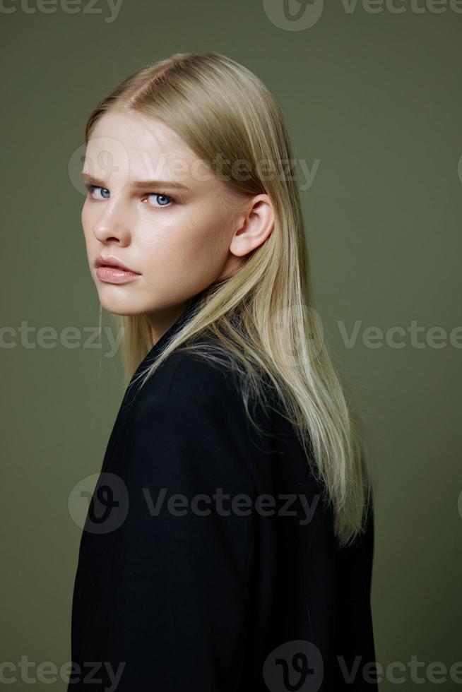 A close portrait of a blonde looking over her shoulder in a black jacket posing in a studio on a green background. The concept of stylish fashion photography photo