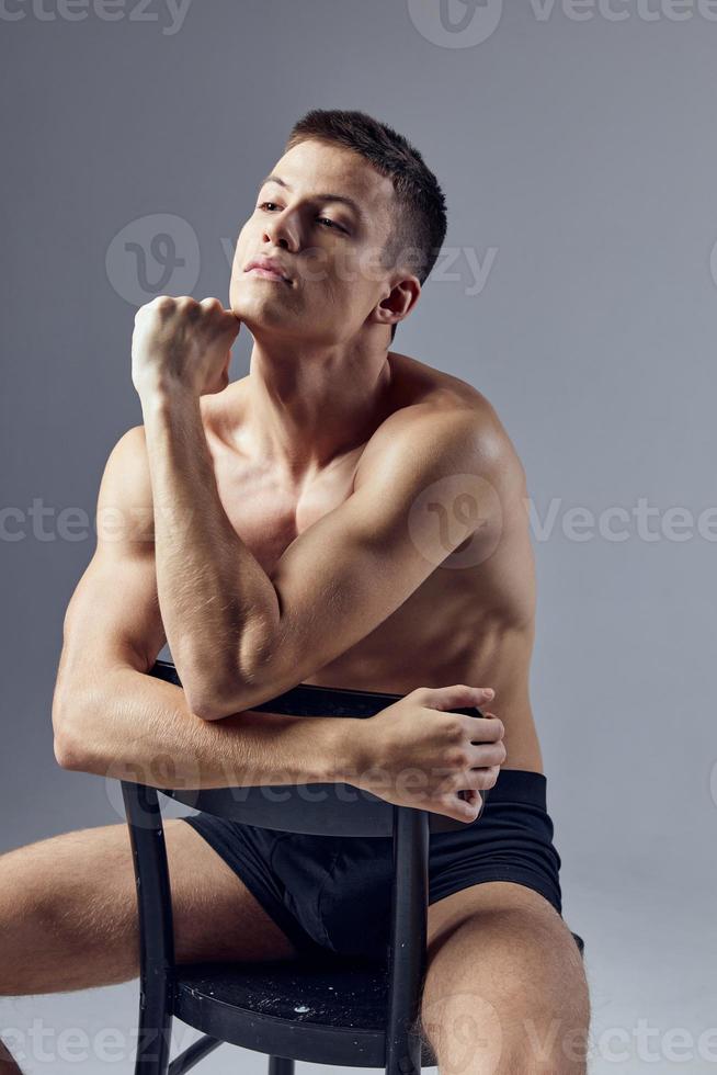 a handsome man with a pumped-up body sits with his elbows on the back of a chair photo