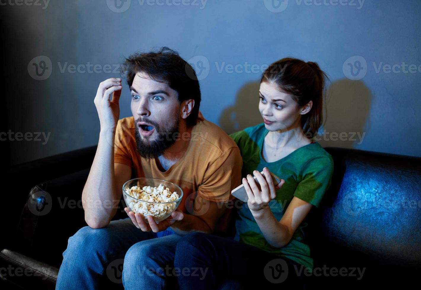a man and a frightened woman watching a movie in the evening on the couch with a plate of popcor photo