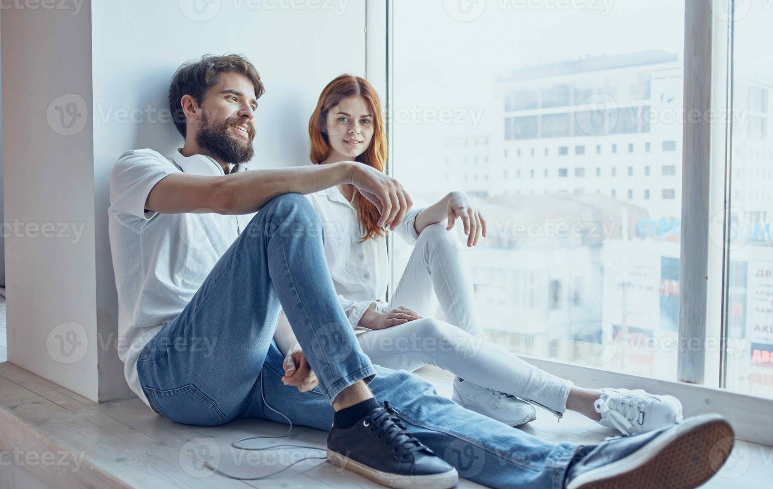 young couple in headphones sitting on the windowsill rest at home photo