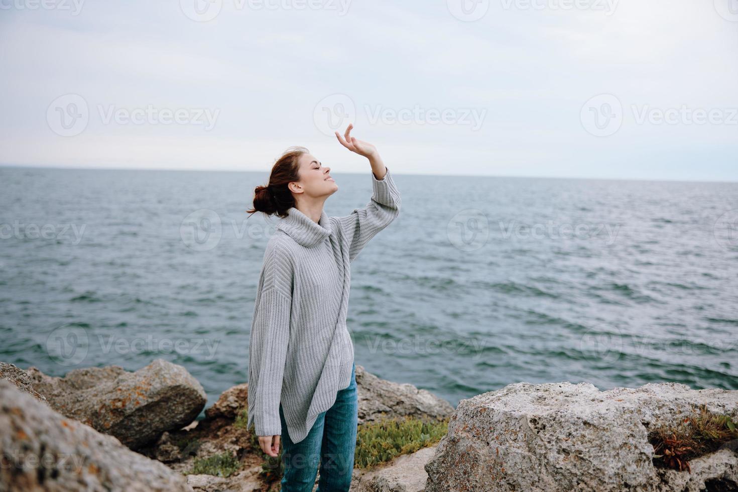 woman in a gray sweater stands on a rocky shore nature Relaxation concept photo