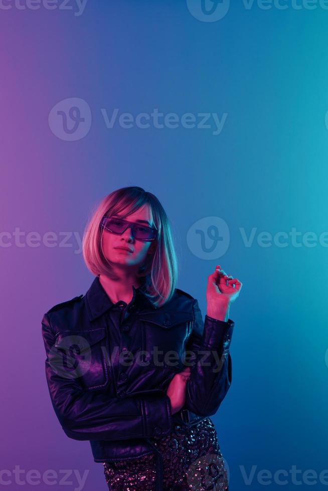 Serious sexy beautiful blonde woman in leather jacket sparkly dress trendy sunglasses fold hands posing isolated in blue pink color light studio background. Neon party Cyberpunk concept. Copy space photo