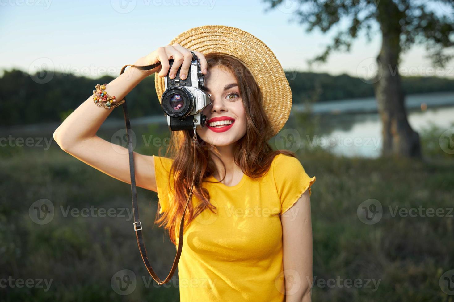 Woman holding camera looks into the camera lens red lips hat nature photo
