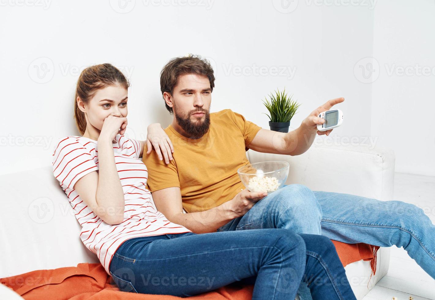 interested woman and bearded man sit on the couch popcorn in a plate and flower in a pot photo