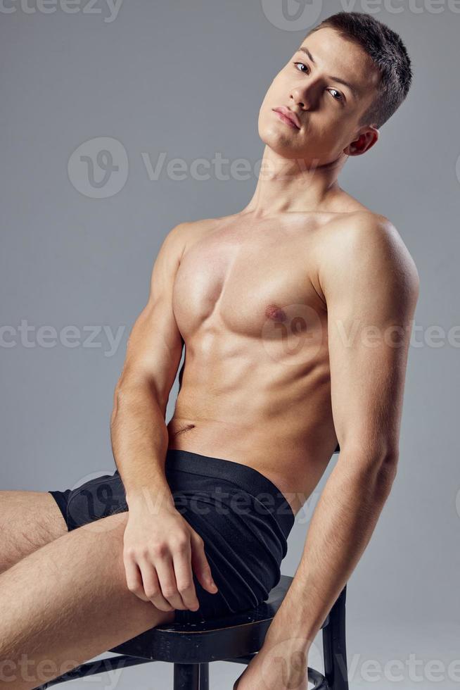 athletic guy with a pumped-up body in black panties sits on a chair rest photo