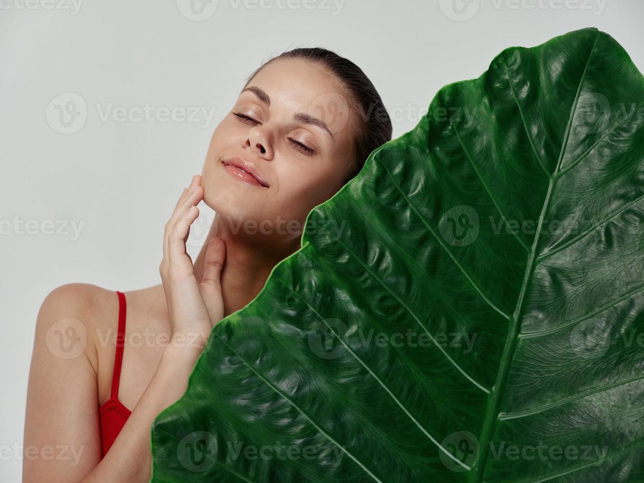 woman with closed eyes touching face with hand and green leaf palm tree clear skin natural look photo