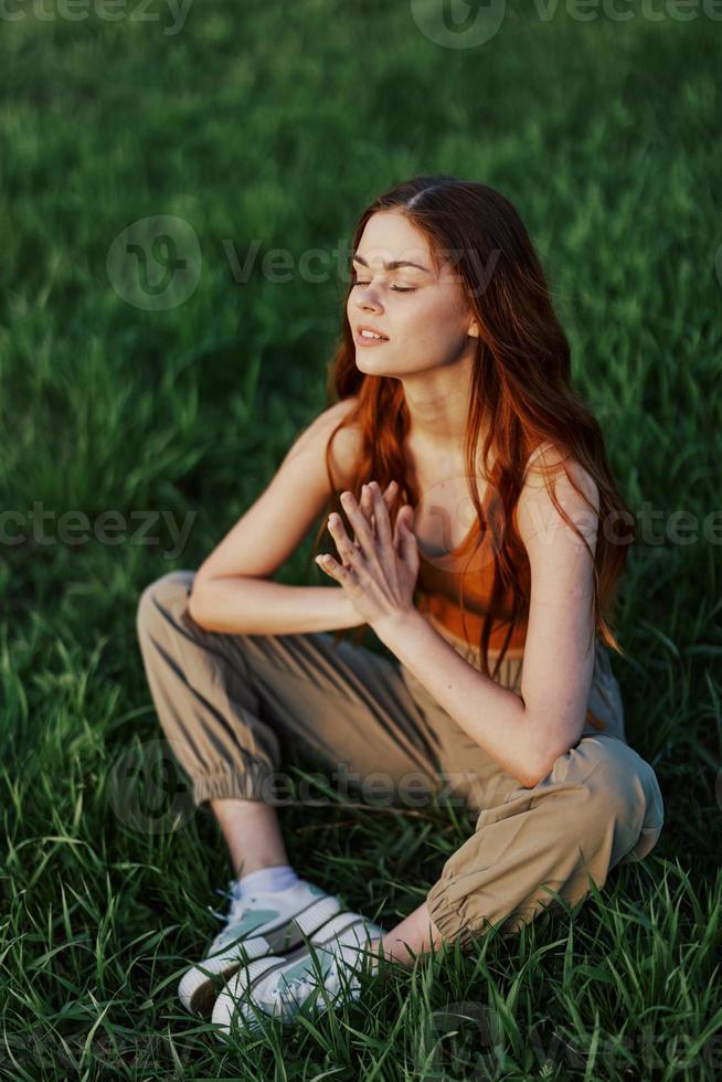 un joven mujer en verano ropa sentado en el verde césped haciendo yoga y meditando en naturaleza, un conexión con el cosmos. el concepto de armonía con cuerpo y naturaleza, espiritual crecimiento foto