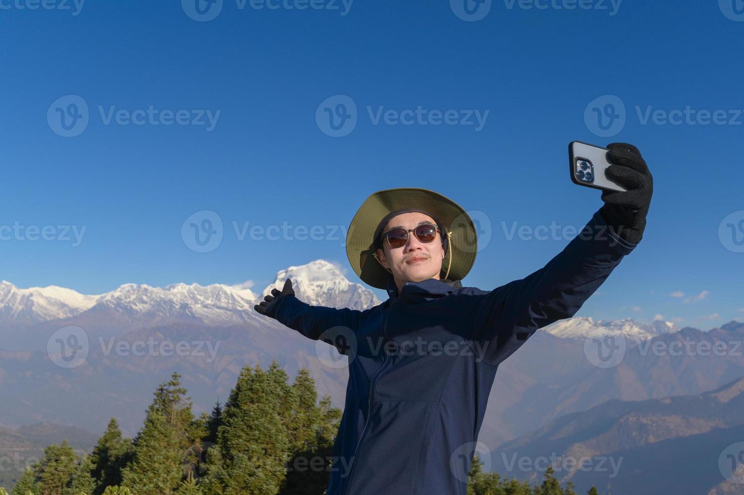 A young traveler takes a selfie or a video call while standing a top a mountain. photo