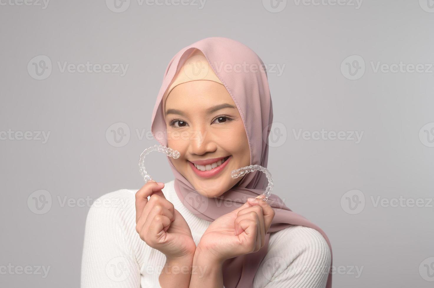 Young smiling muslim woman with hijab holding invisalign braces in studio, dental healthcare and Orthodontic concept photo