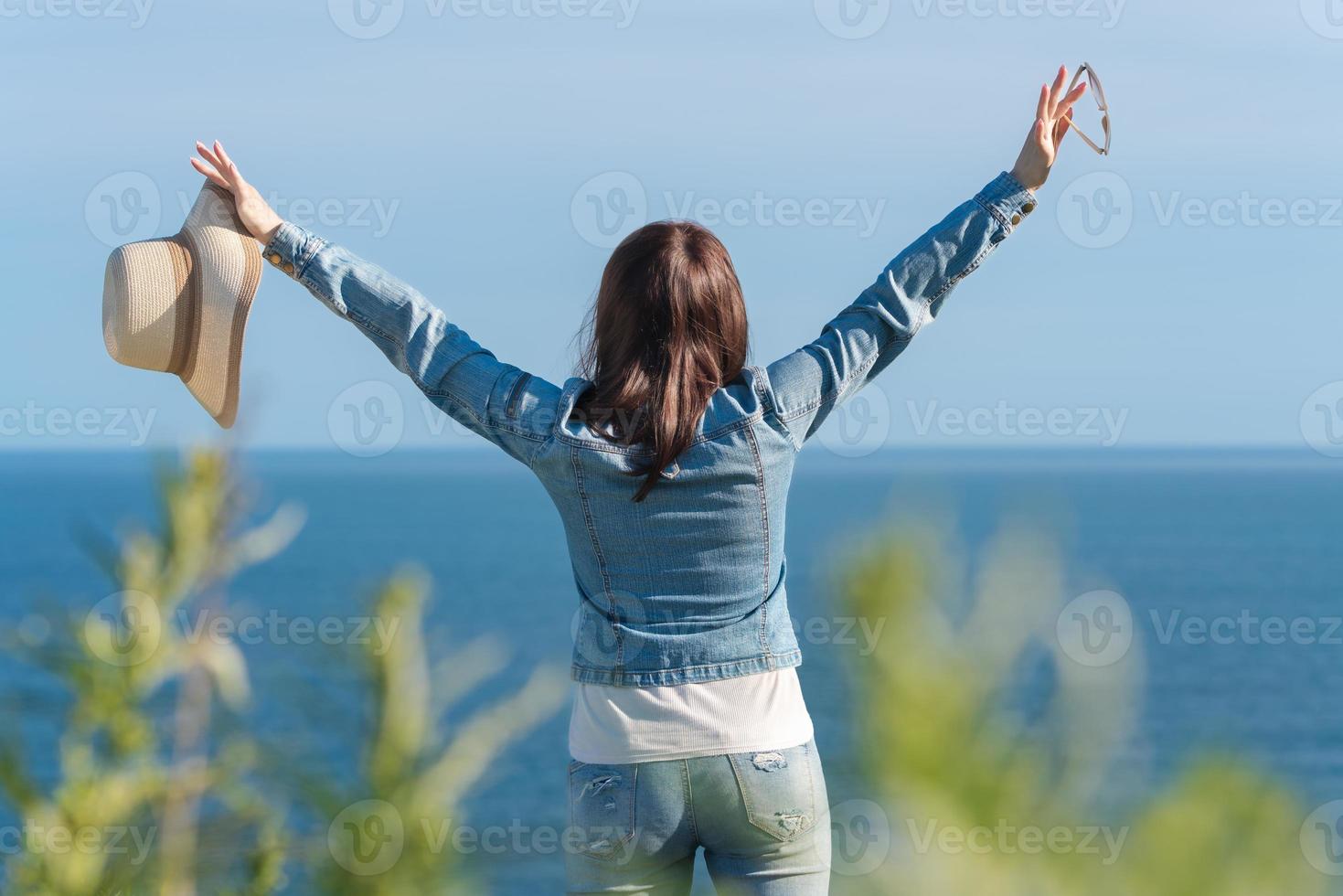 Rear view of unrecognizable woman raised hands, holding straw hat in one hand, sunglasses in other photo