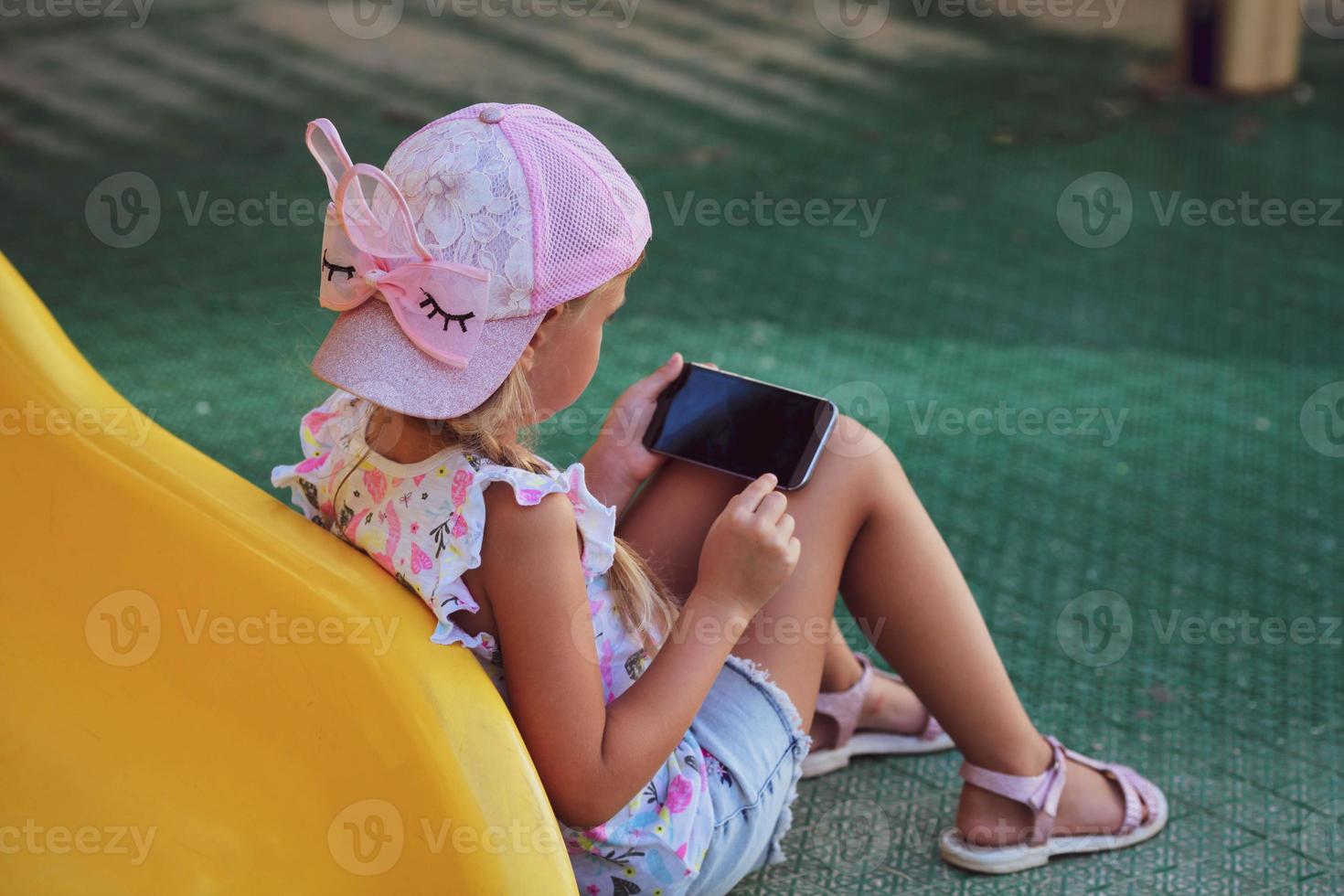 The girl sits on the playground and plays games on the phone. Internet addiction, loneliness. photo