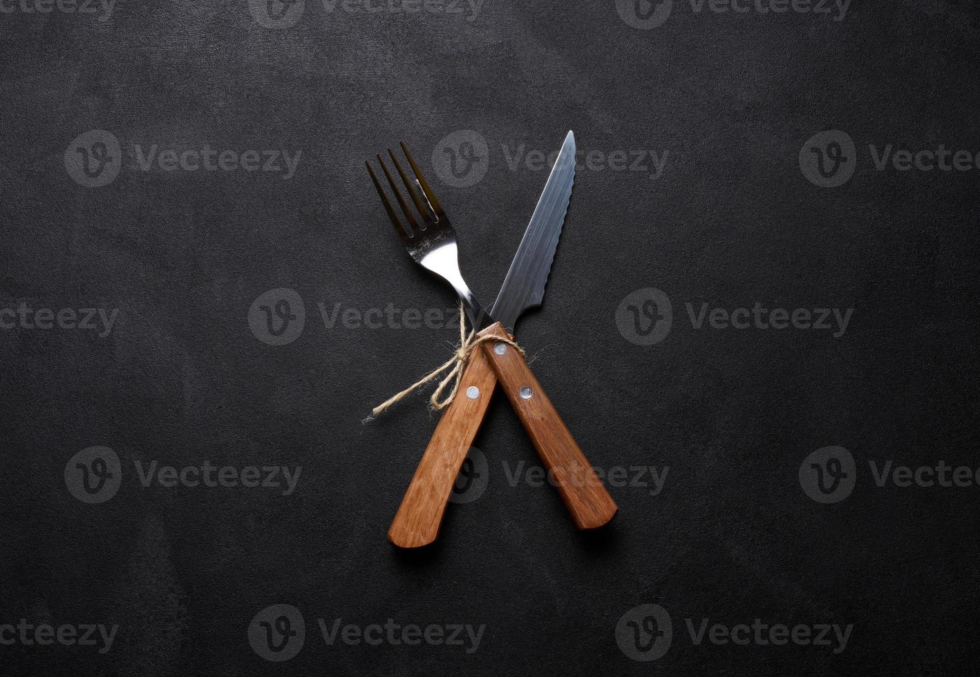 Fork and knife with wooden handle on black background, top view photo