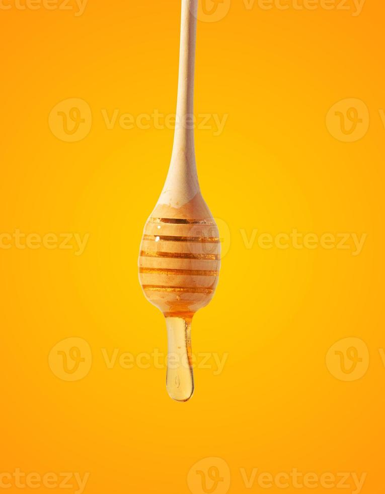 Flowing drops of yellow honey from a wooden stick on a yellow background photo