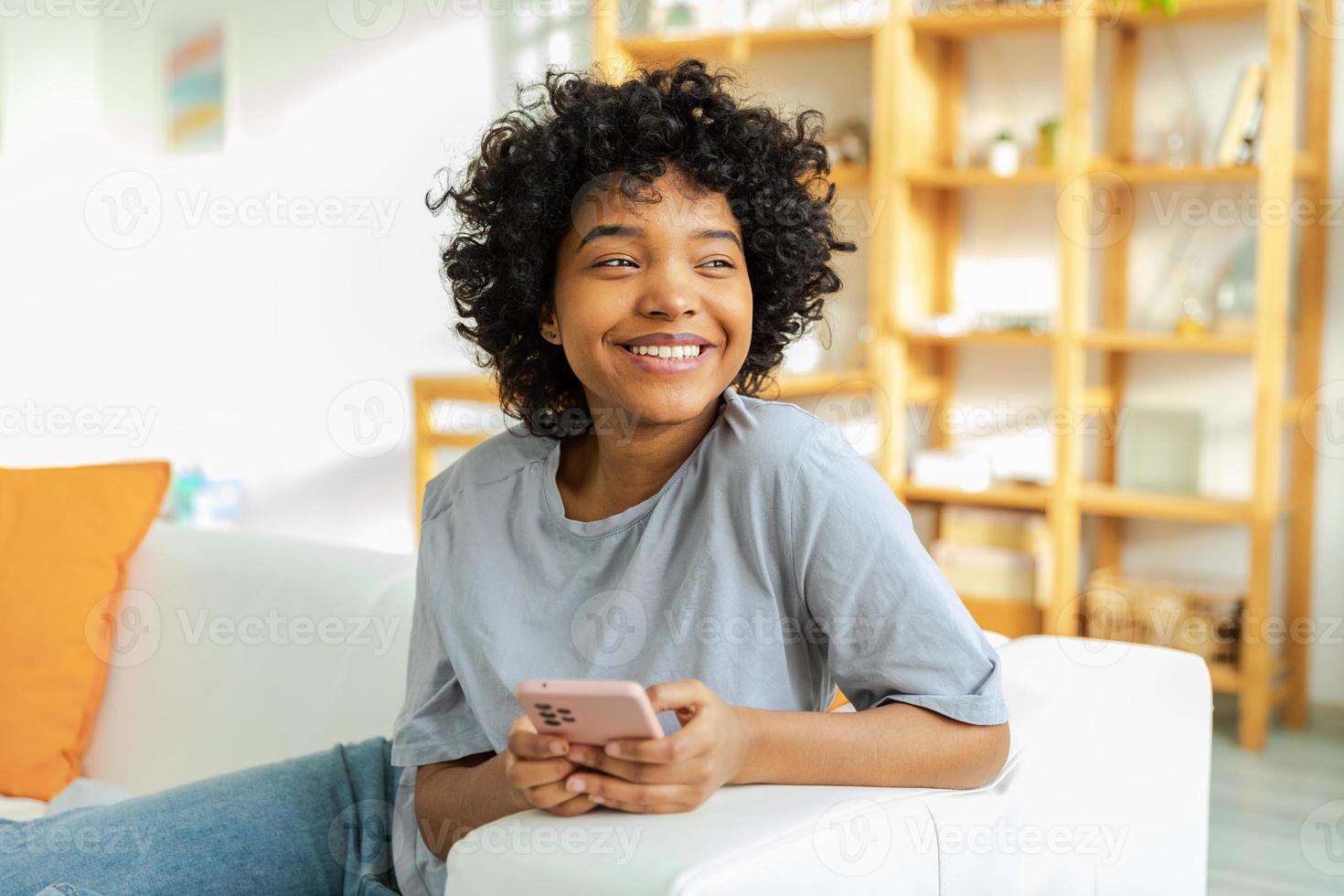 African girl holding smartphone touch screen typing scroll page at home. Woman with cell phone surfing internet using social media apps playing game. Shopping online Internet news cellphone addiction. photo
