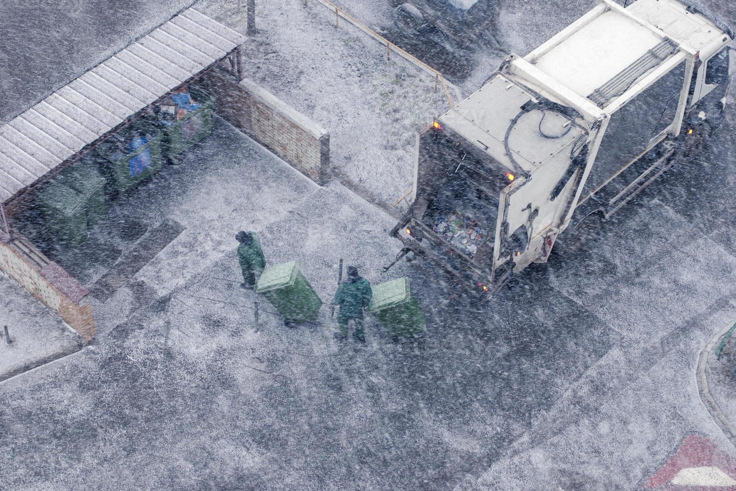 Garbage truck and workers in snow storm, top view photo