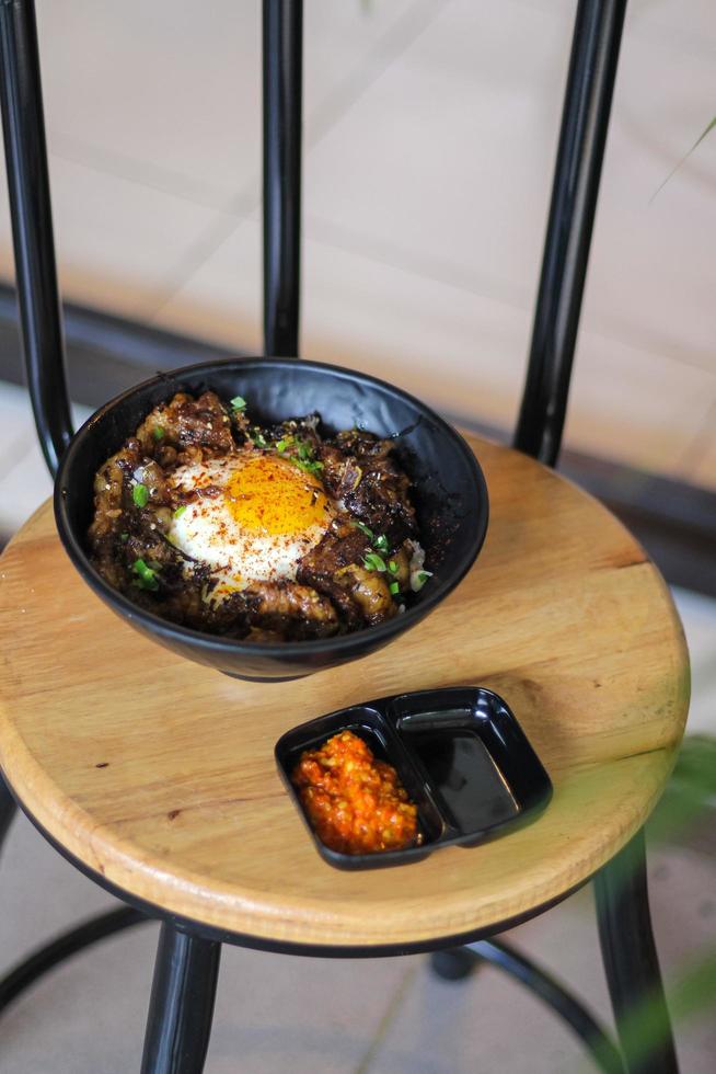 Rice topped with beef and egg on a wooden table in a restaurant photo
